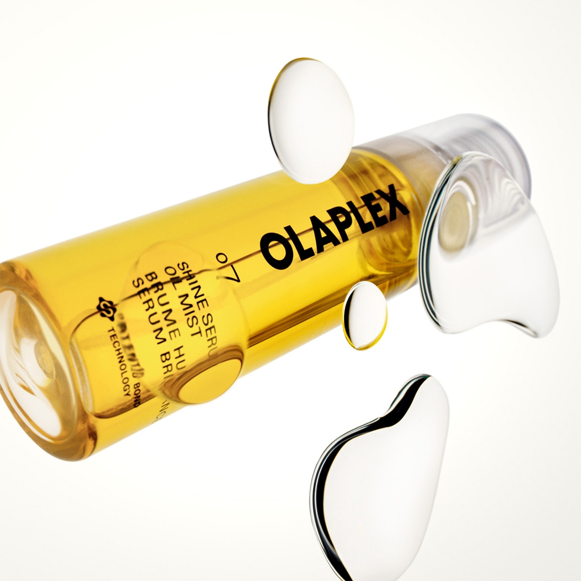 Olaplex N°7 Bonding Oil, un olio leggero e trasparente con una formula brevettata per capelli lucidi e sani, è mostrato in una bottiglia trasparente con etichetta nera e bianca, circondata da goccioline d'acqua.
