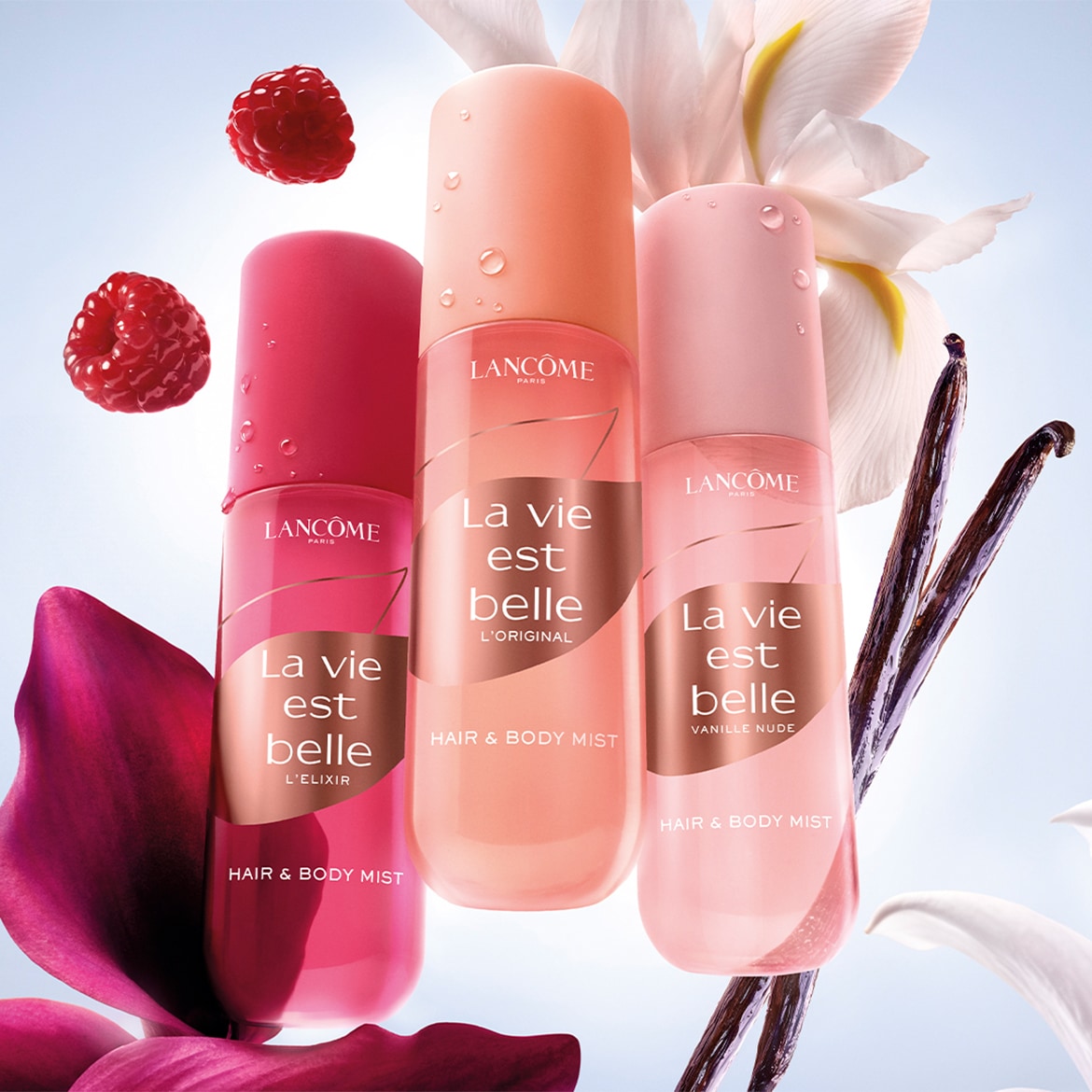 Tre flaconi di La Vie Est Belle Hair & Body Mist di Lancôme in rosa, pesca e rosso, con lamponi, fiori bianchi e baccelli di vaniglia.