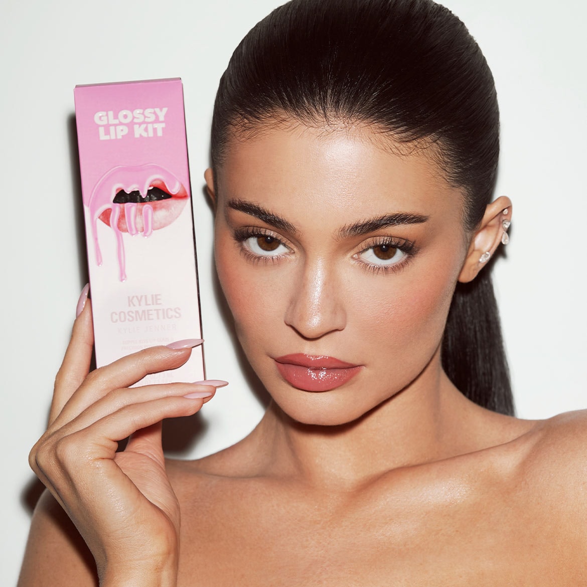 Una modella tiene in mano un kit labbra lucido di Kylie Cosmetics, con una confezione rosa decorata con labbra gocciolanti, per labbra perfette e brillanti.