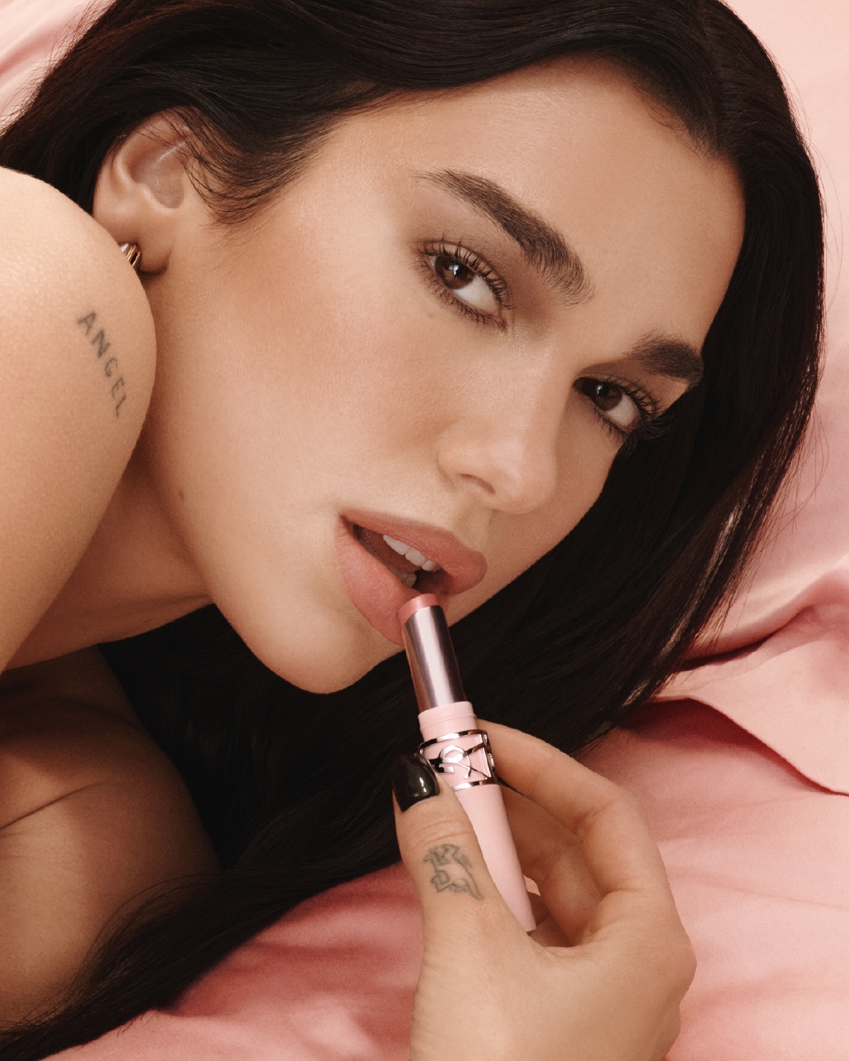 Primo piano di una donna che applica un rossetto rosa chiaro sulle labbra, con confezione rosa e dettagli argentati.