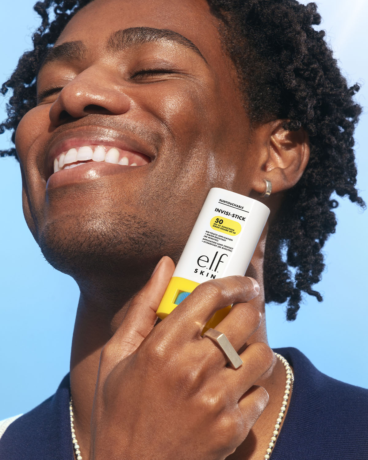 Un uomo sorridente applica lo stick solare SPF 50 di e.l.f. SKIN, che offre un'applicazione senza contatto e resistenza all'acqua per 80 minuti.