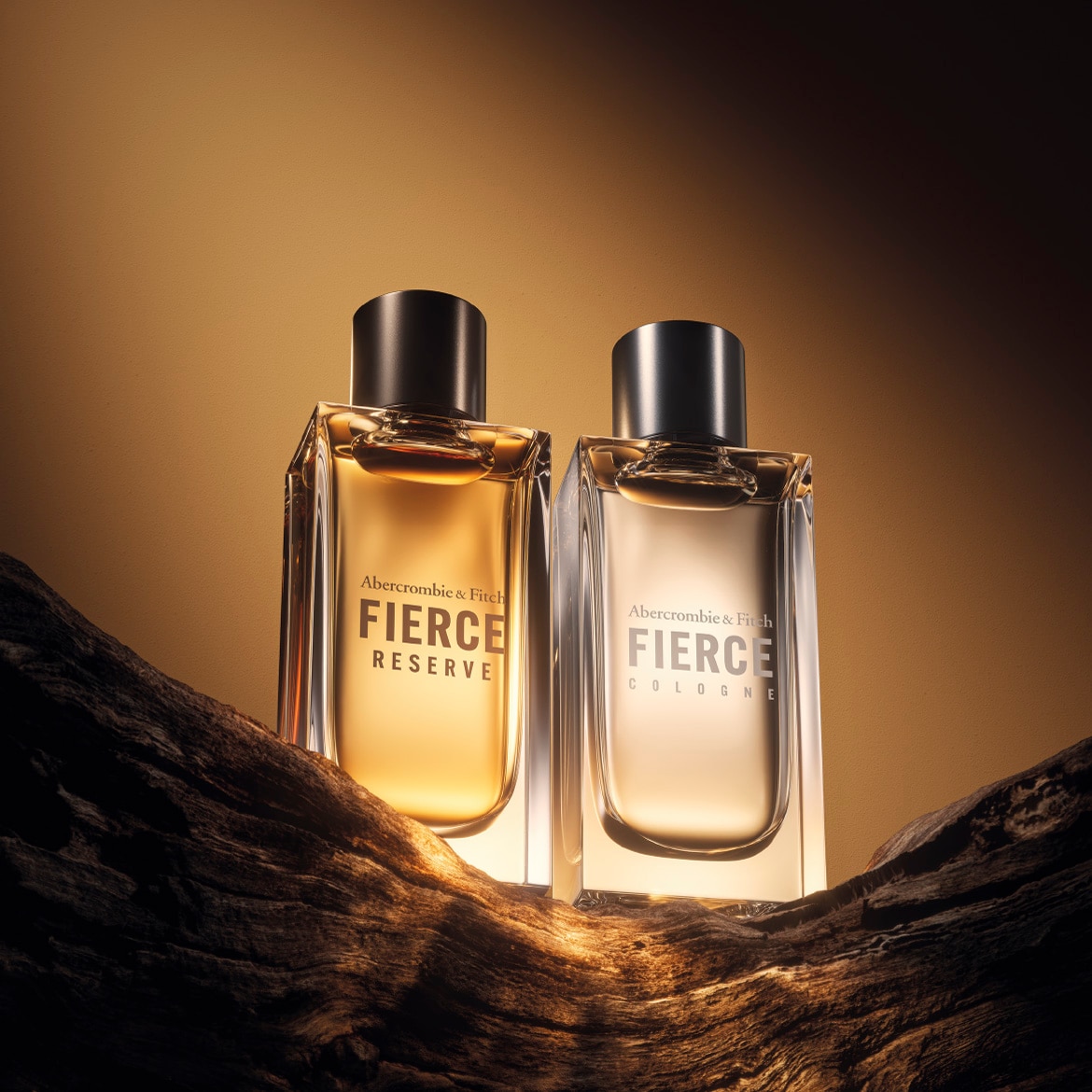 Ecco due flaconi di profumo Abercrombie & Fitch Fierce, uno Reserve color ambrato e l'altro Cologne color argento, su una superficie ruvida di legno scuro.
