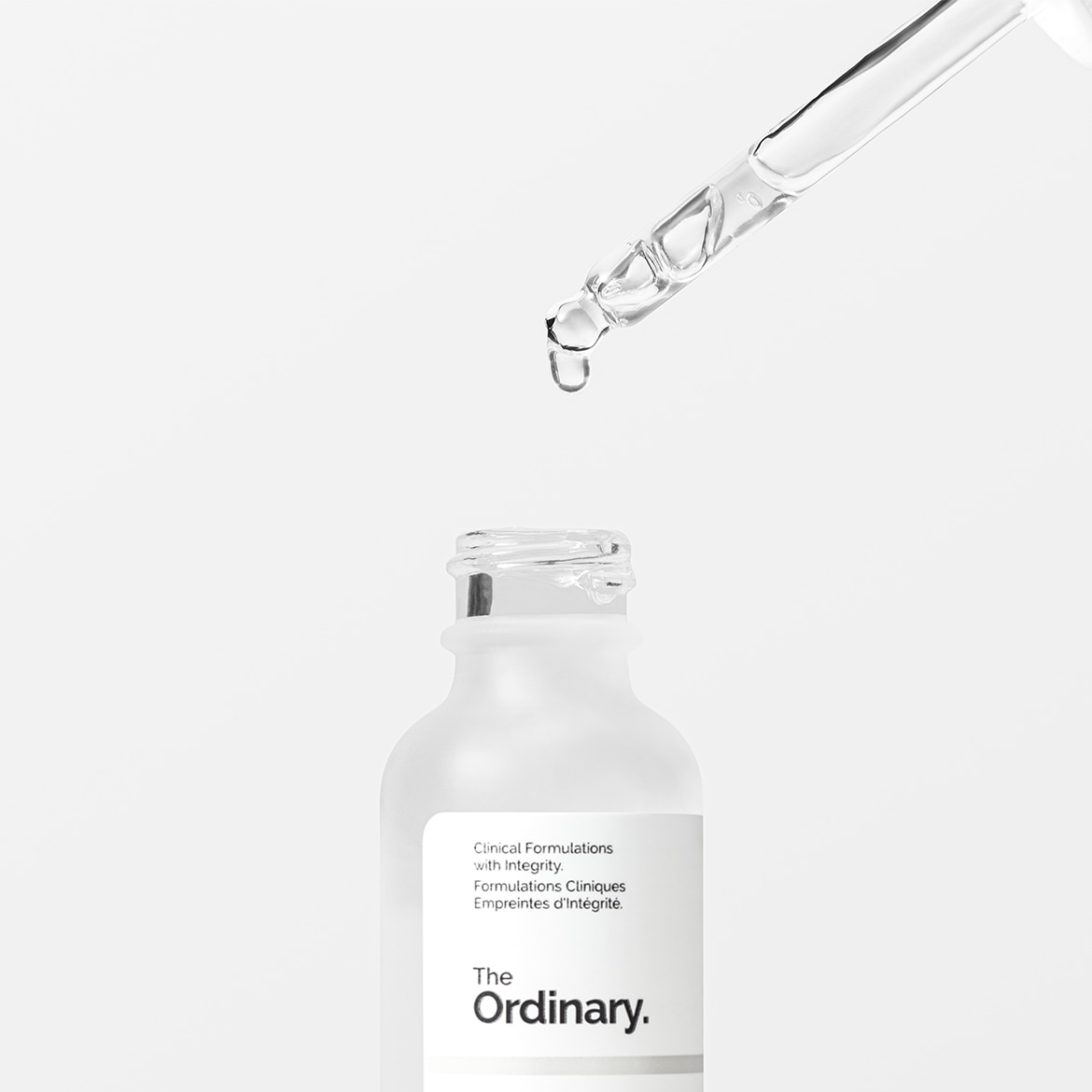 Flacone bianco opaco di The Ordinary con contagocce trasparente che rilascia una goccia di siero, per un trattamento viso mirato.