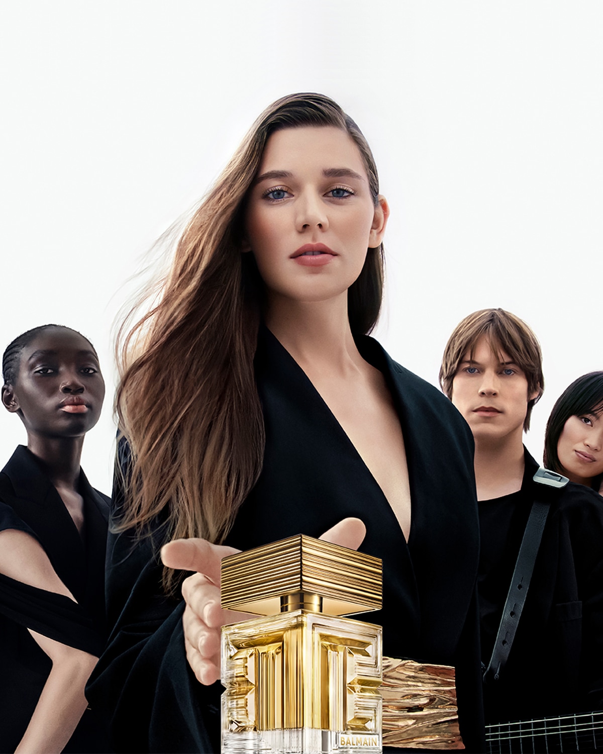 Una donna tiene in mano una bottiglia di profumo dorata Balmain con altre persone dietro, che mostra l'eleganza e il lusso della fragranza.