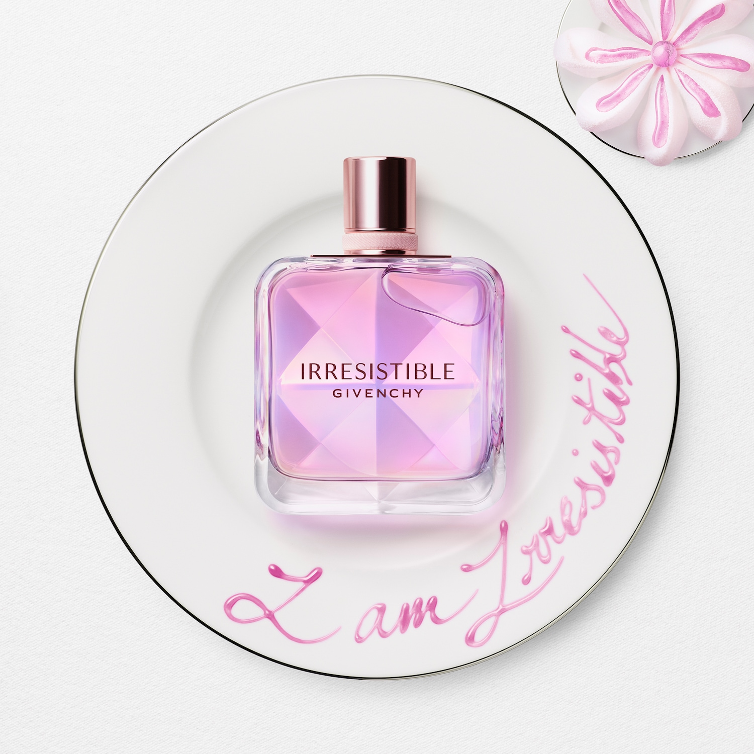Il profumo Givenchy Irresistibile, con il suo flacone sfaccettato rosa e tappo color oro rosa, è adagiato su un piatto bianco con la scritta rosa "I am Irresistible".