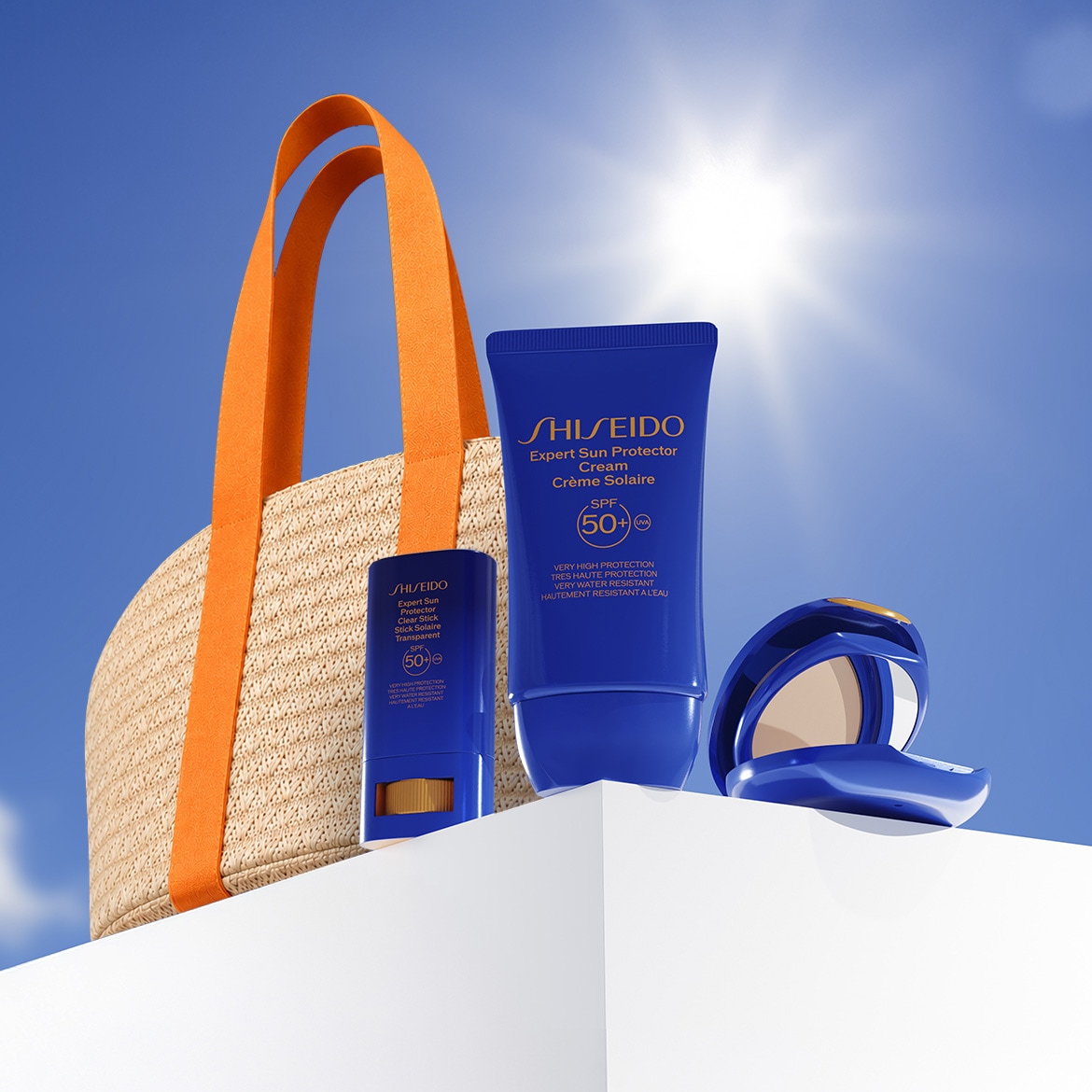 Sullo sfondo di un cielo azzurro e un sole splendente, borsa da spiaggia in paglia con manici arancioni, crema solare Shiseido Expert Sun Protector blu e stick trasparente SPF 50+.