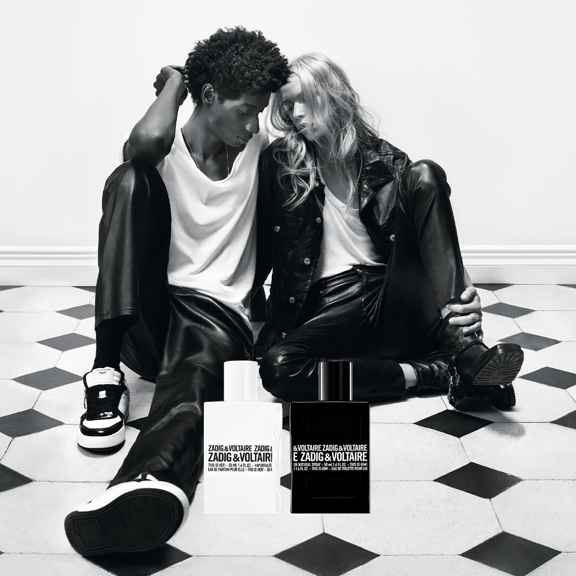 In un'immagine in bianco e nero, una coppia è seduta sul pavimento a scacchi con i profumi Zadig & Voltaire "This is Her!" e "This is Him!".