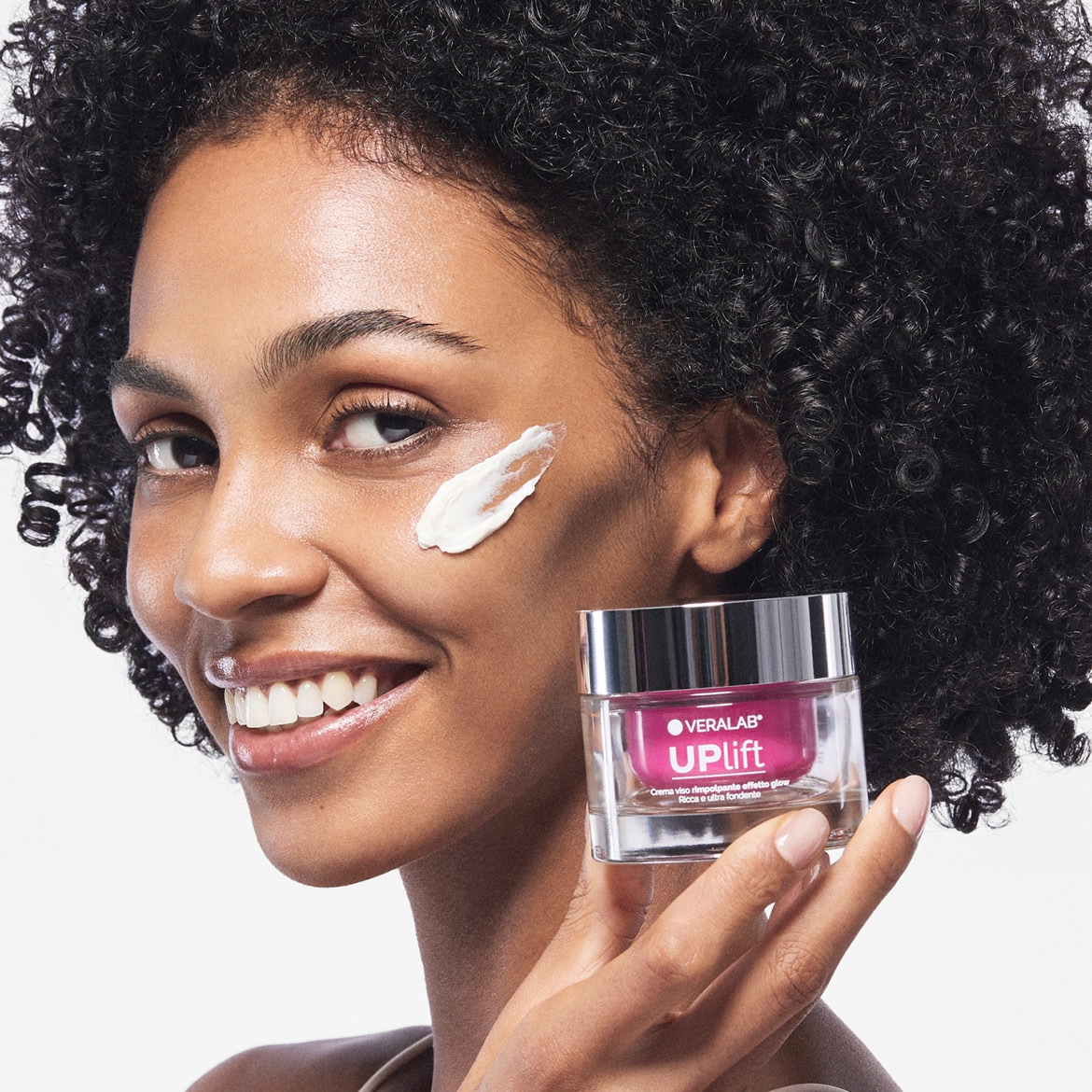 Una donna sorridente applica la crema Verlab UP Lift sul viso, mostrando la texture ricca e ultra fondente per un effetto glow.