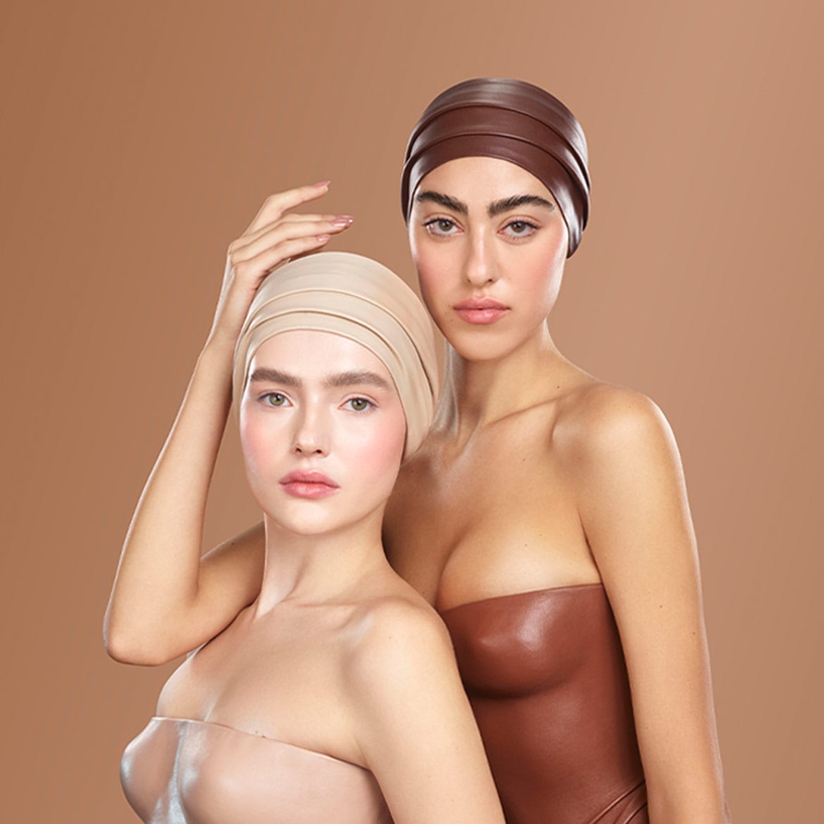 Due donne con turbanti color crema e marrone posano con un trucco naturale e una carnagione impeccabile.