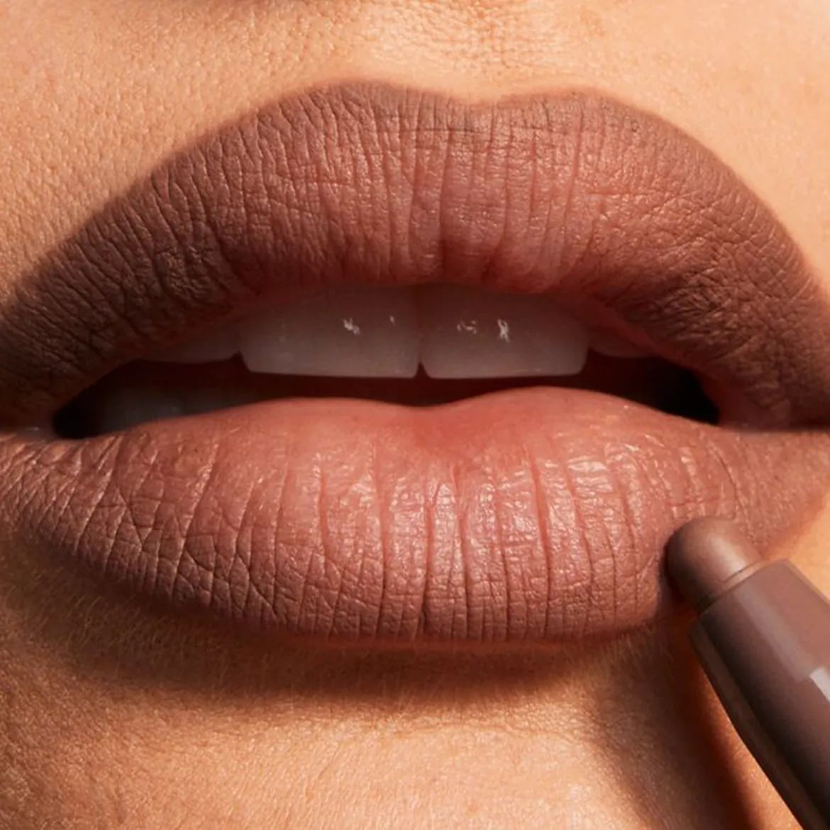 Un rossetto marrone opaco viene applicato sulle labbra, creando un look audace e sofisticato.