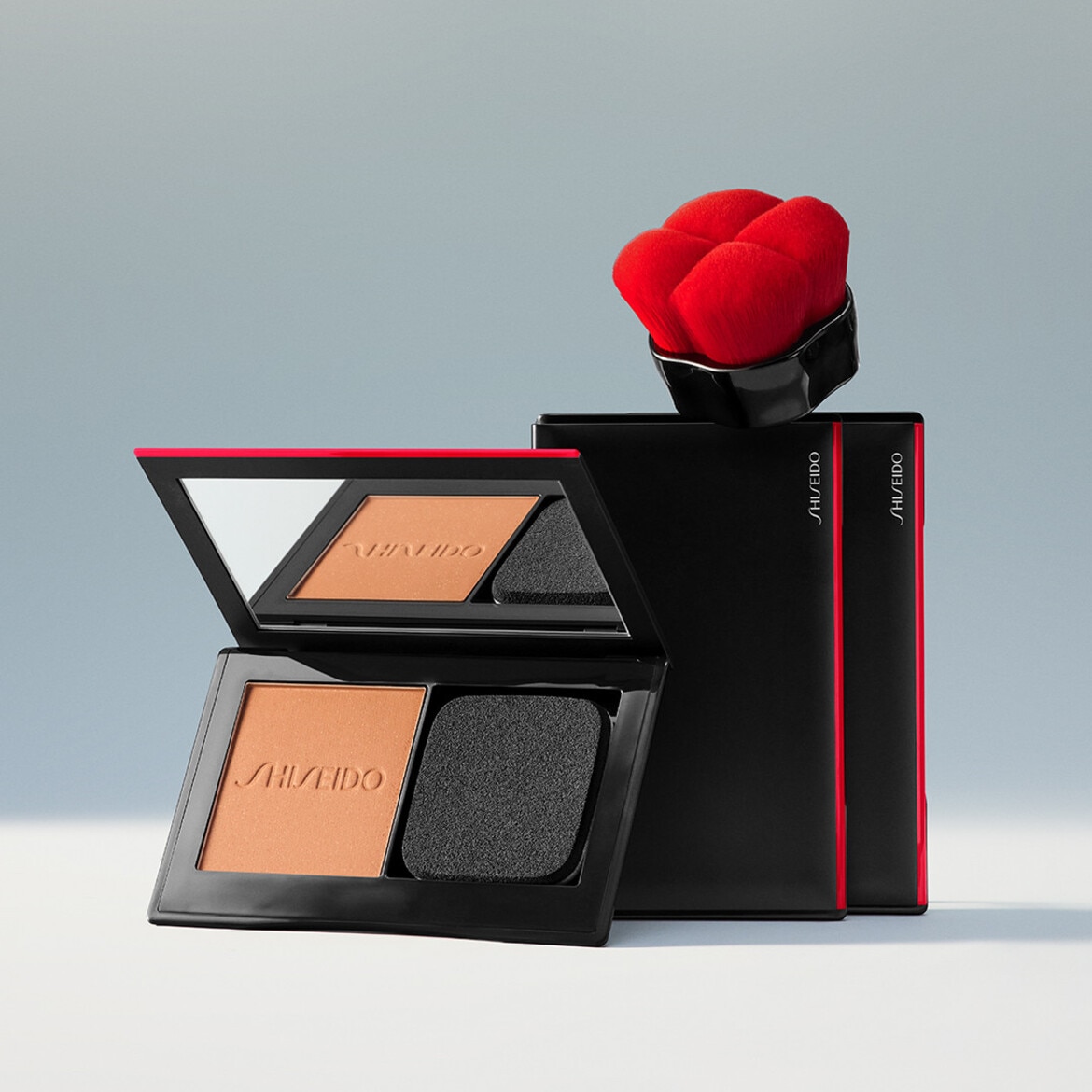 Ecco la cipria Shiseido in una confezione nera con dettagli rossi, completa di specchio, spugnetta nera e pennello rosso per un'applicazione impeccabile.