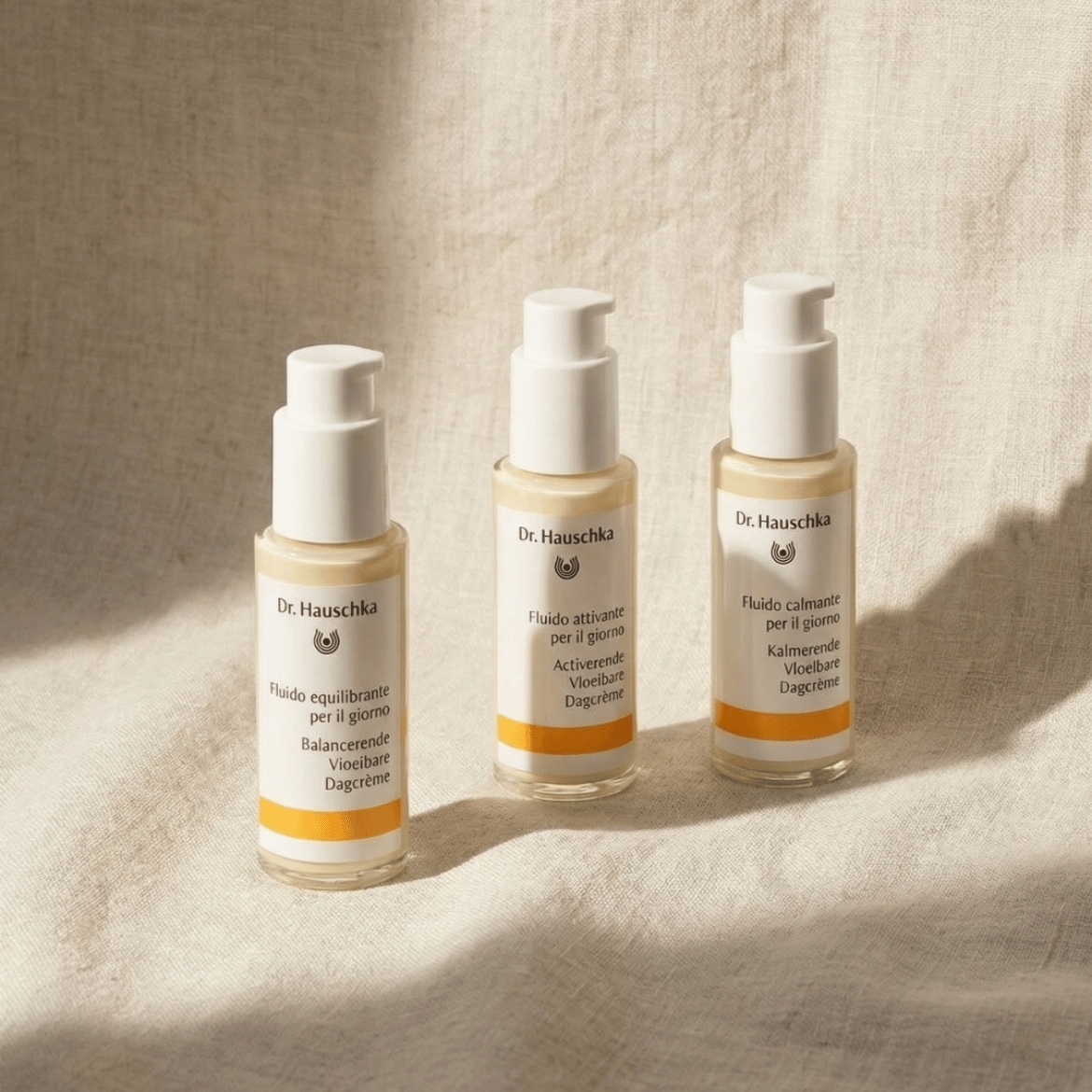 Tre flaconi di crema Dr. Hauschka, ognuno con etichette che indicano "Fluido equilibrante", "Fluido attivante" e "Fluido calmante" per il giorno, ideali per la cura quotidiana della pelle.