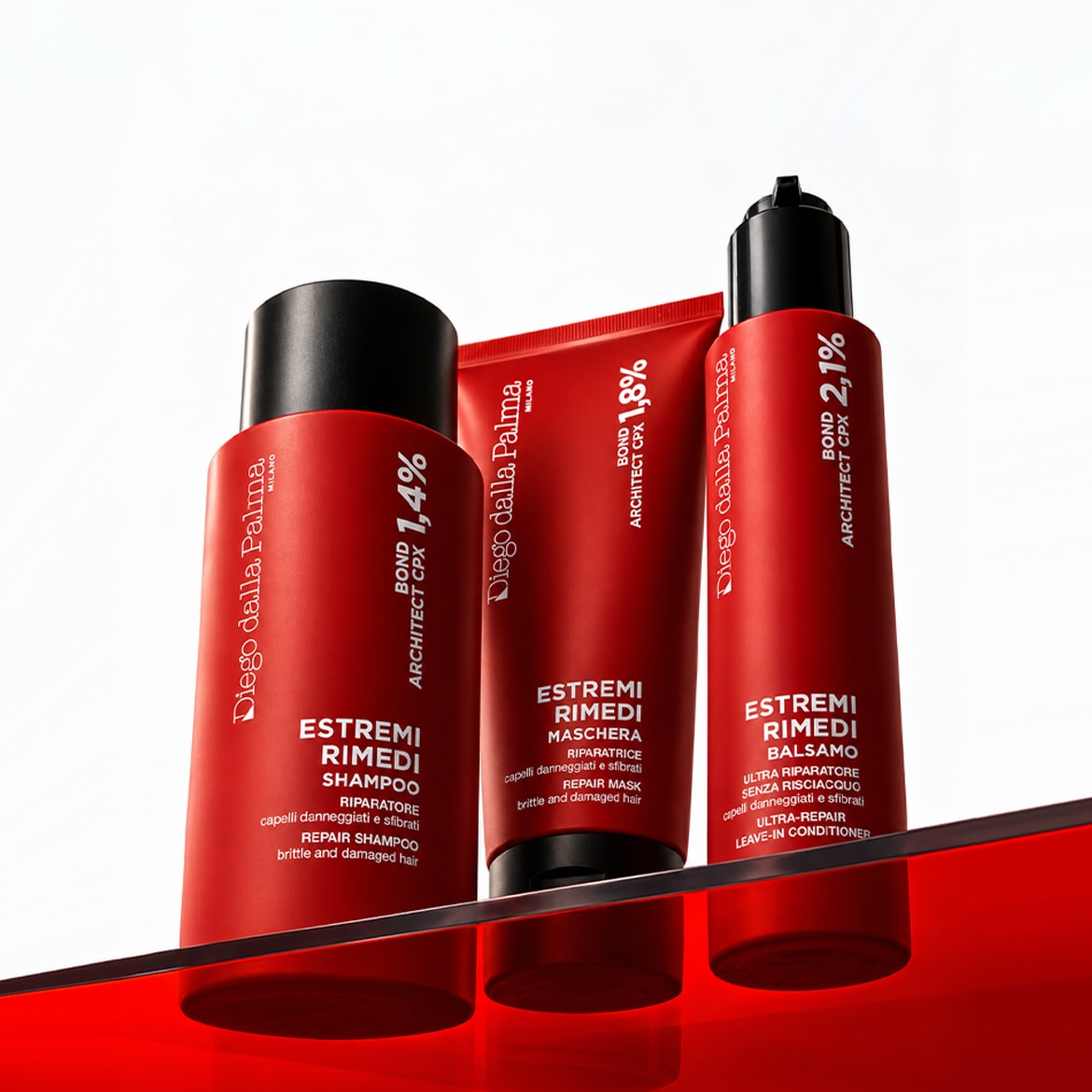 Tre prodotti Diego dalla Palma Estremi Rimedi, uno shampoo, una maschera e un balsamo senza risciacquo, sono esposti su una superficie rossa lucida, con etichette che indicano "BOND ARCHITECT CPX" e percentuali di 1,4%, 1,8% e 2,1%.