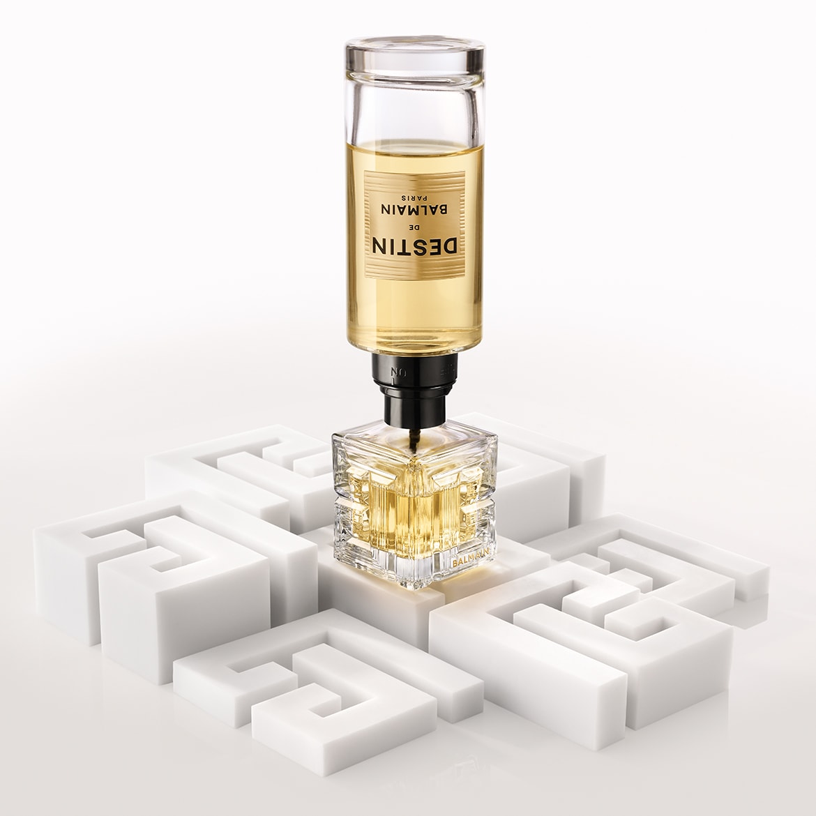 Ecco il profumo Balmain in un flacone di vetro trasparente con tappo dorato, adagiato accanto a una peonia rosa e fragole mature, evocando una fragranza lussuosa e fruttata.