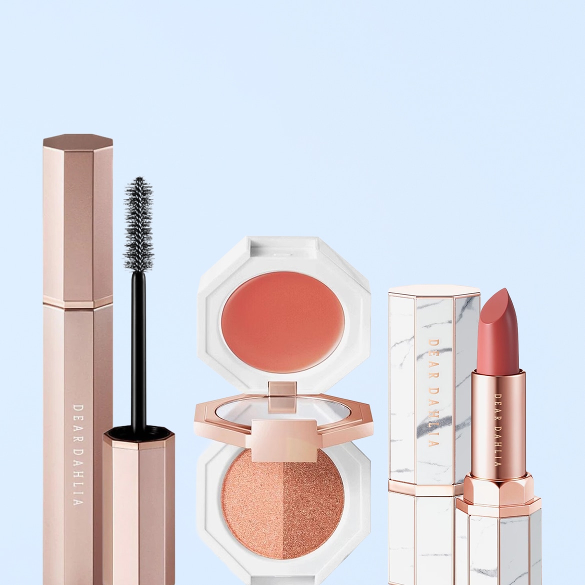 Ecco un set di cosmetici Dear Dahlia con mascara dal packaging color bronzo, blush e ombretto compatti color pesca e un rossetto color corallo.