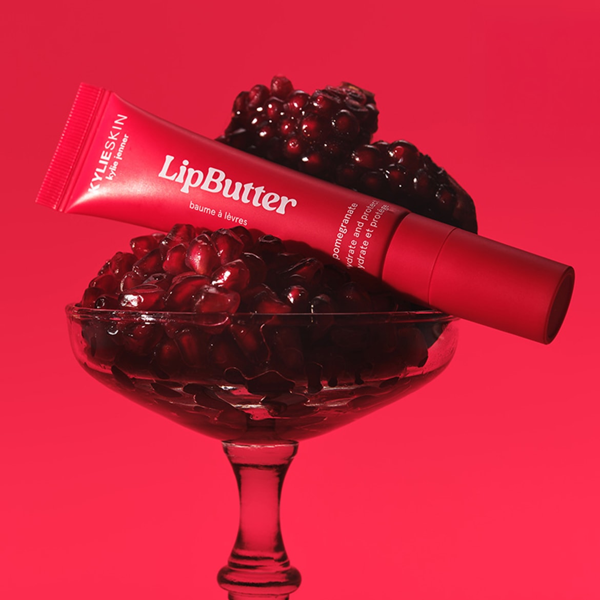 Il LipButter di KylieSkin in un tubo rosso, adagiato su un calice pieno di chicchi di melograno, promette idratazione e protezione per le labbra.
