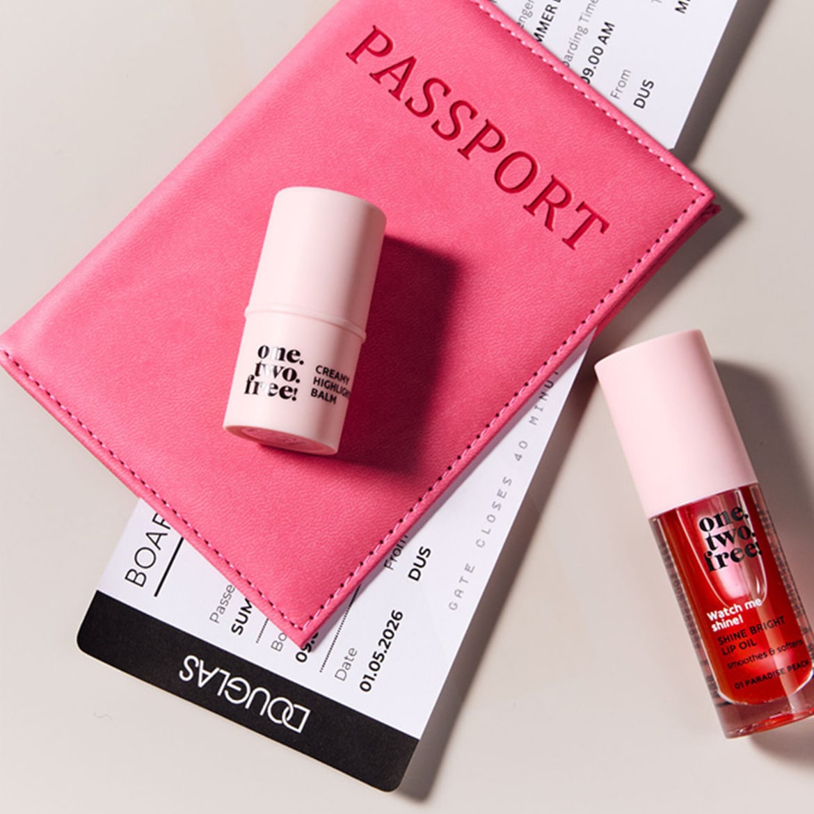 Ecco un set di bellezza essenziale per il tuo prossimo viaggio: un balsamo illuminante cremoso e un olio labbra brillante, presentati con un passaporto rosa e una carta d'imbarco.