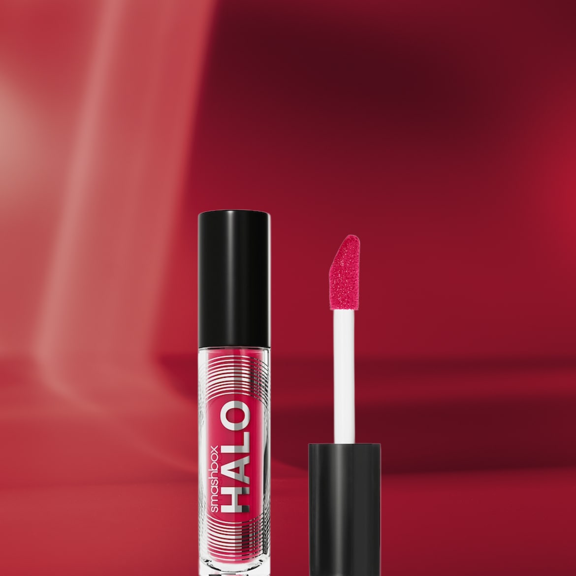 Ecco il lucidalabbra Smashbox Halo in una confezione trasparente con tappo nero e applicatore bianco, che mostra una formula lucida e vibrante color ciliegia.