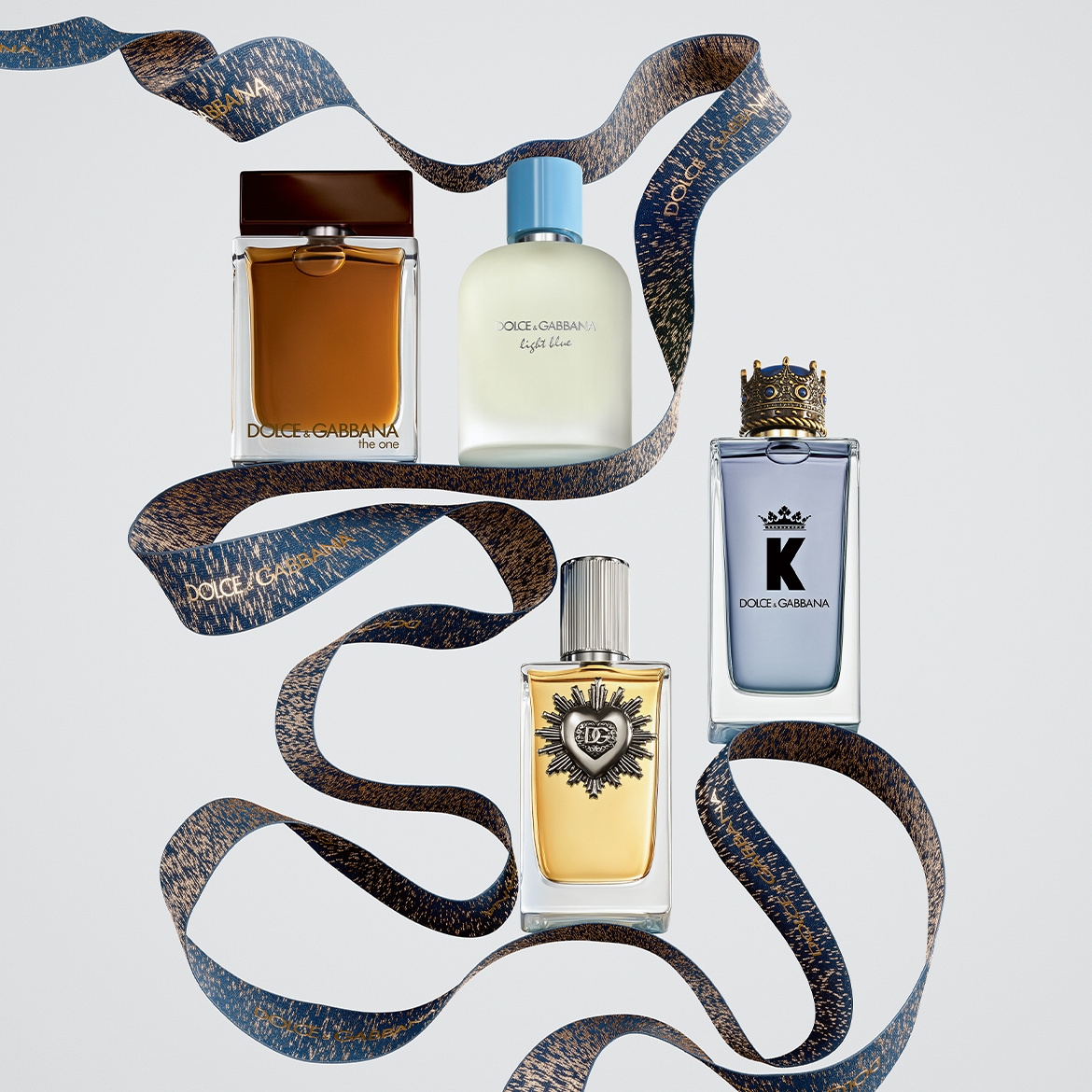 Scopri la collezione di profumi Dolce&Gabbana: The One, Light Blue, K e il profumo con il cuore sacro, avvolti da un nastro decorativo blu e oro.