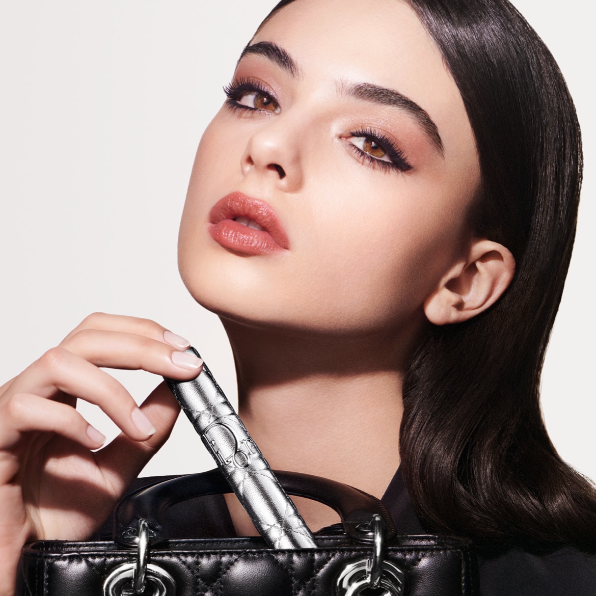 Primo piano di una modella con un rossetto color pesca e un mascara argentato Dior, che aggiunge un tocco di lusso al suo look.