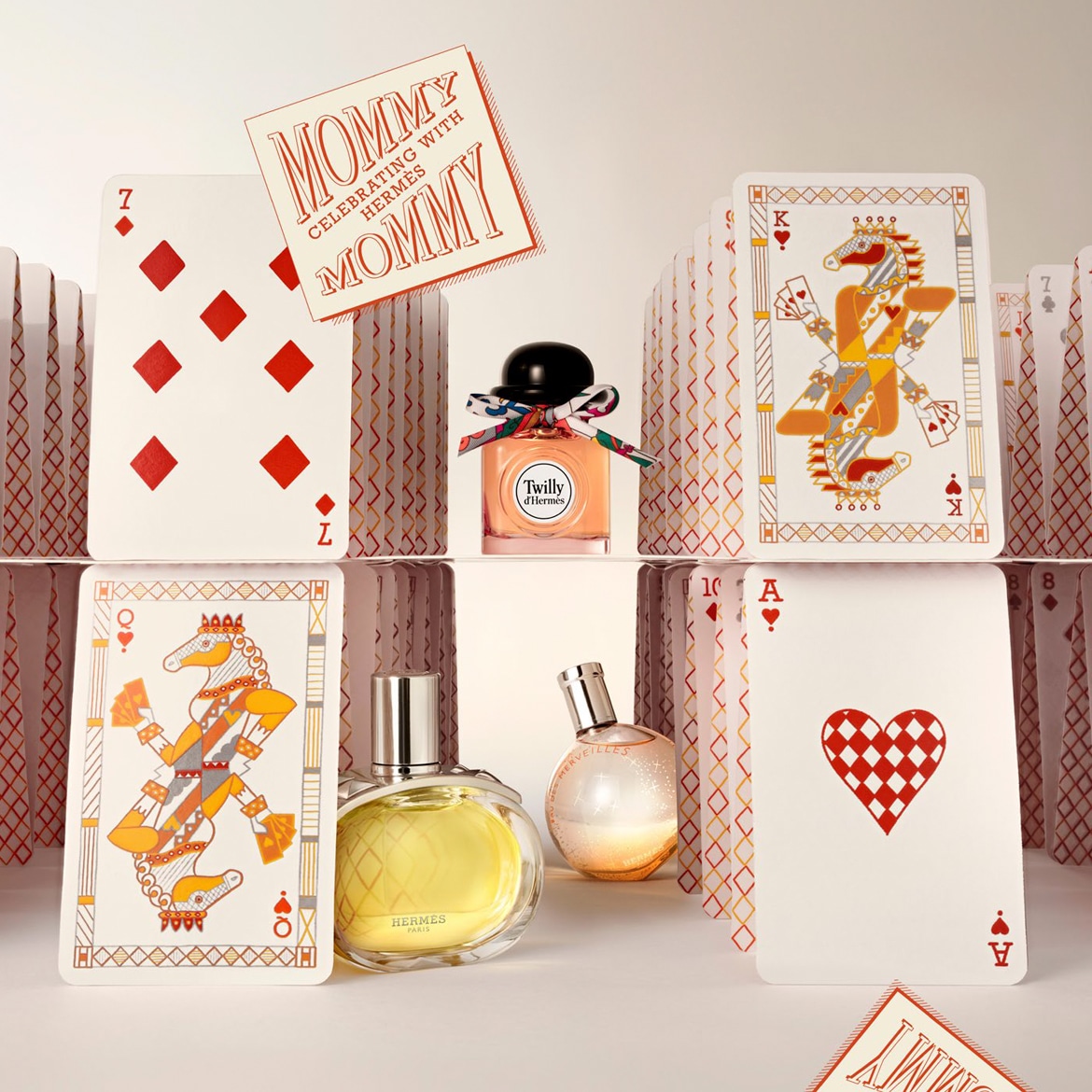 Festeggia la mamma con Hermès: scopri Twilly d'Hermès, un profumo in un flacone arancione con un fiocco colorato, circondato da carte da gioco.