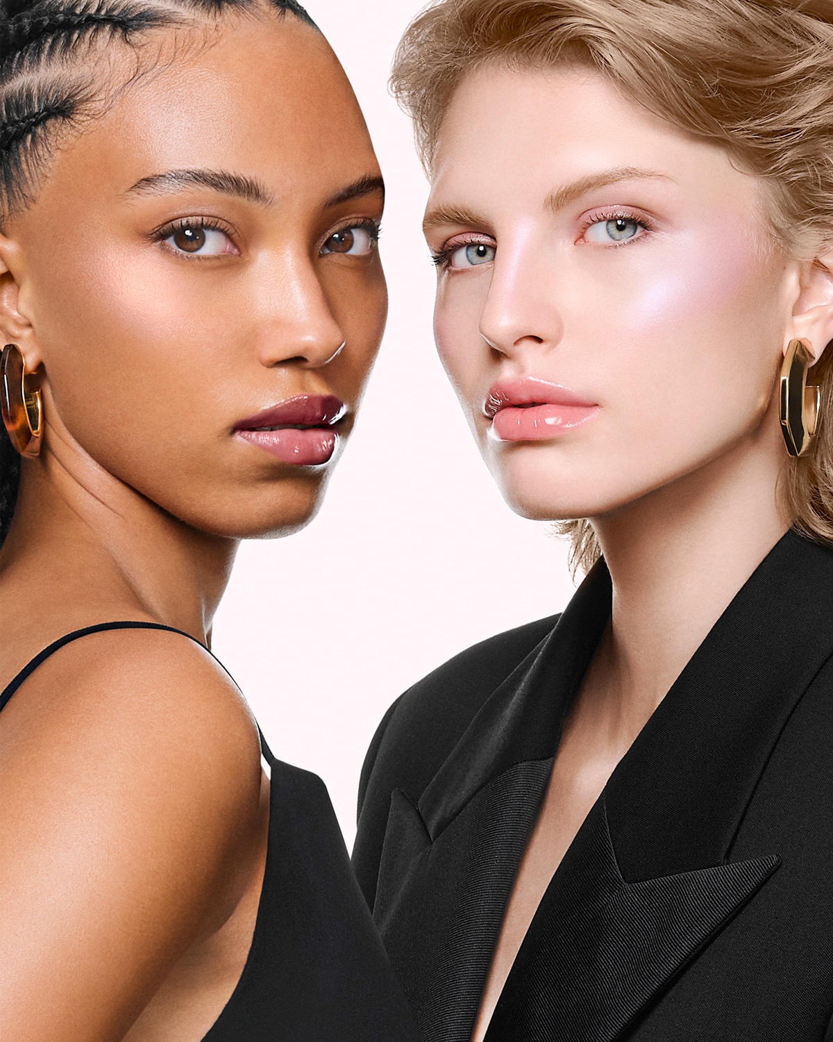 Primo piano di due donne con incarnati diversi, che indossano un blazer nero e orecchini dorati, con labbra lucide e trucco luminoso.