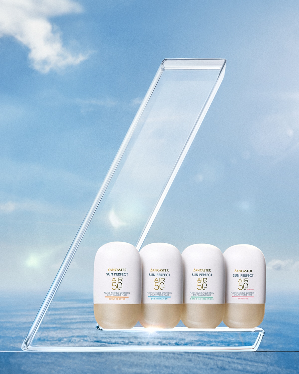 Quattro flaconi di protezione solare Lancaster Sun Perfect Air 50 con diverse proprietà, tra cui glow booster, idratazione 24 ore, pori e imperfezioni e sensitive, presentati su un espositore trasparente.