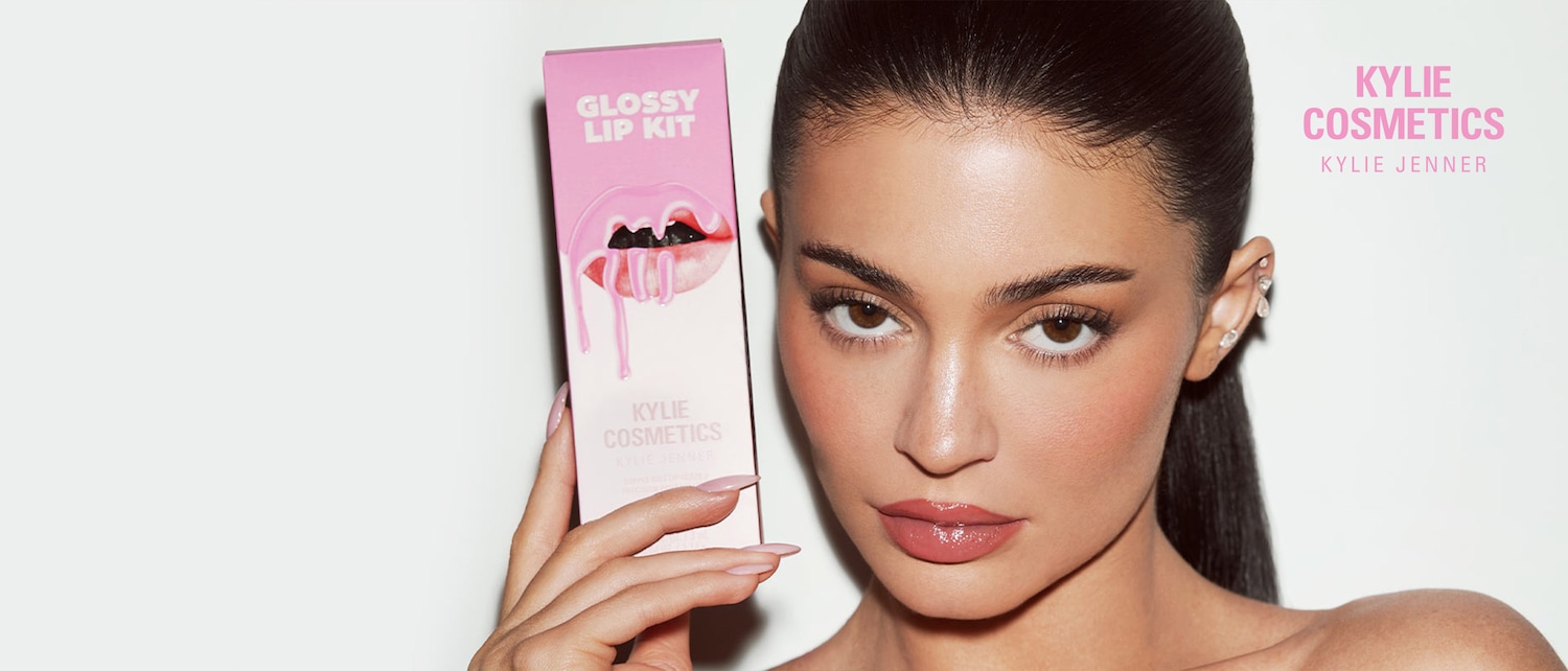 Ecco il kit labbra lucide di Kylie Cosmetics, tenuto in mano da Kylie Jenner, con labbra rosa lucide e gocciolanti sulla confezione.