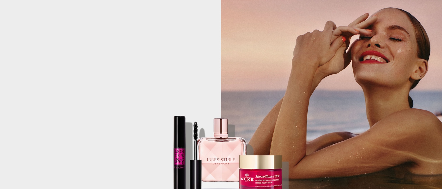 Una selezione di prodotti di bellezza: mascara nero Lancôme Monsieur Big, profumo Givenchy Irresistible in flacone rosa e crema viso Nuxe Merveillance Lift in vasetto rosso.