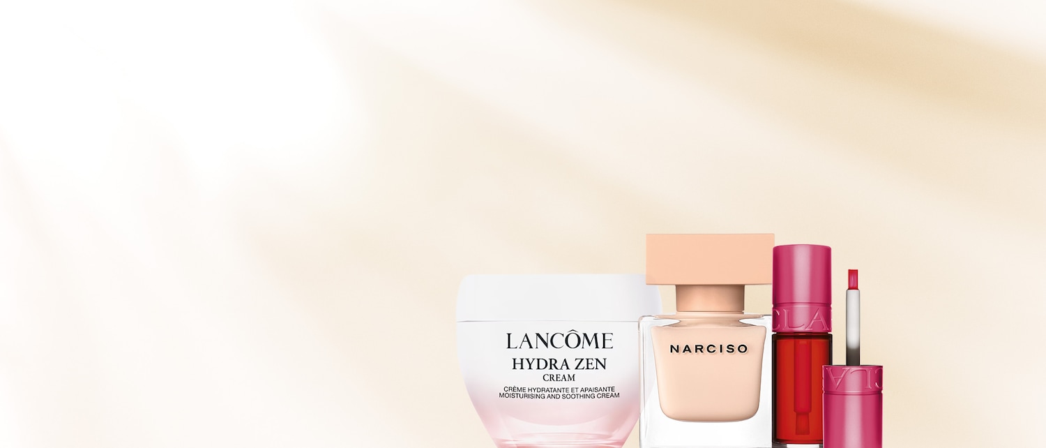 Primo piano di Lancôme Hydra Zen Cream, Narciso profumo e Clarins Lip Comfort Oil in tonalità rosa su sfondo beige chiaro.