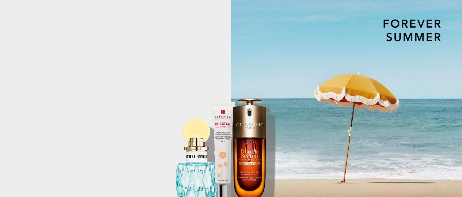 La foto mostra una collezione di prodotti di bellezza, tra cui un profumo azzurro, una BB cream Erborian e il siero Double Serum di Clarins, sullo sfondo di una spiaggia assolata con la scritta "FOREVER SUMMER".