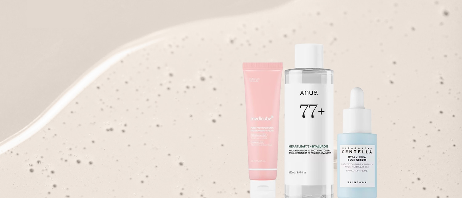 Tre prodotti per la cura della pelle sono allineati su uno sfondo chiaro con bolle: una crema idratante rosa Medicube, un tonico Anua Heartleaf 77+ Hyaluron e un siero blu Skin1004 Madagascar Centella Hyalu-Cica.