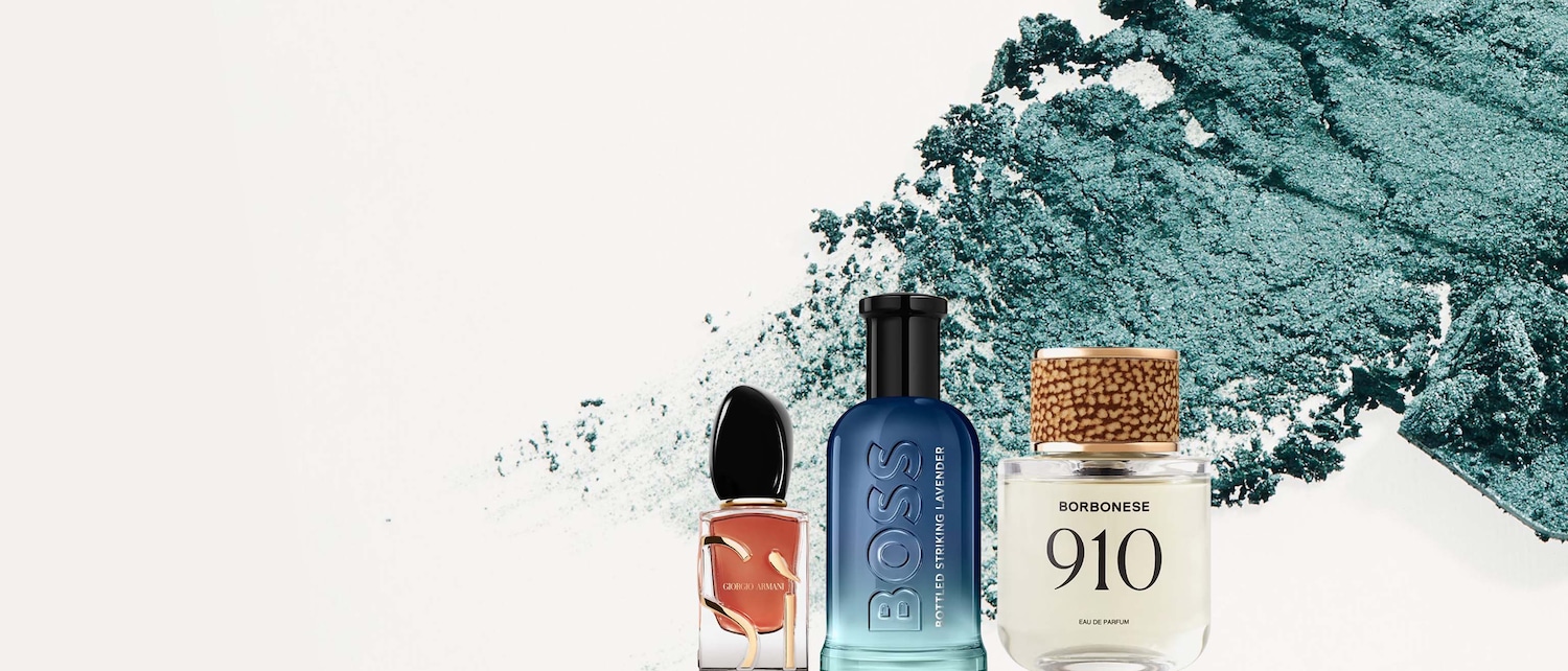 Tre flaconi di profumo di diverse marche, tra cui Giorgio Armani, Boss e Borbonese, sono esposti su uno sfondo bianco con una spruzzata di polvere verde acqua.