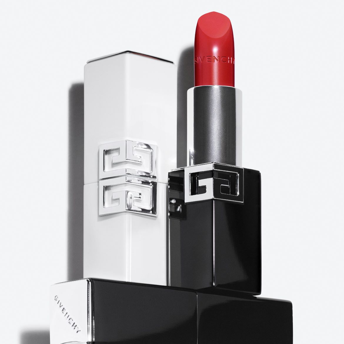 Un rossetto rosso brillante con il logo Givenchy in rilievo è mostrato in un elegante astuccio nero e argento, con un astuccio bianco e argento abbinato sullo sfondo.