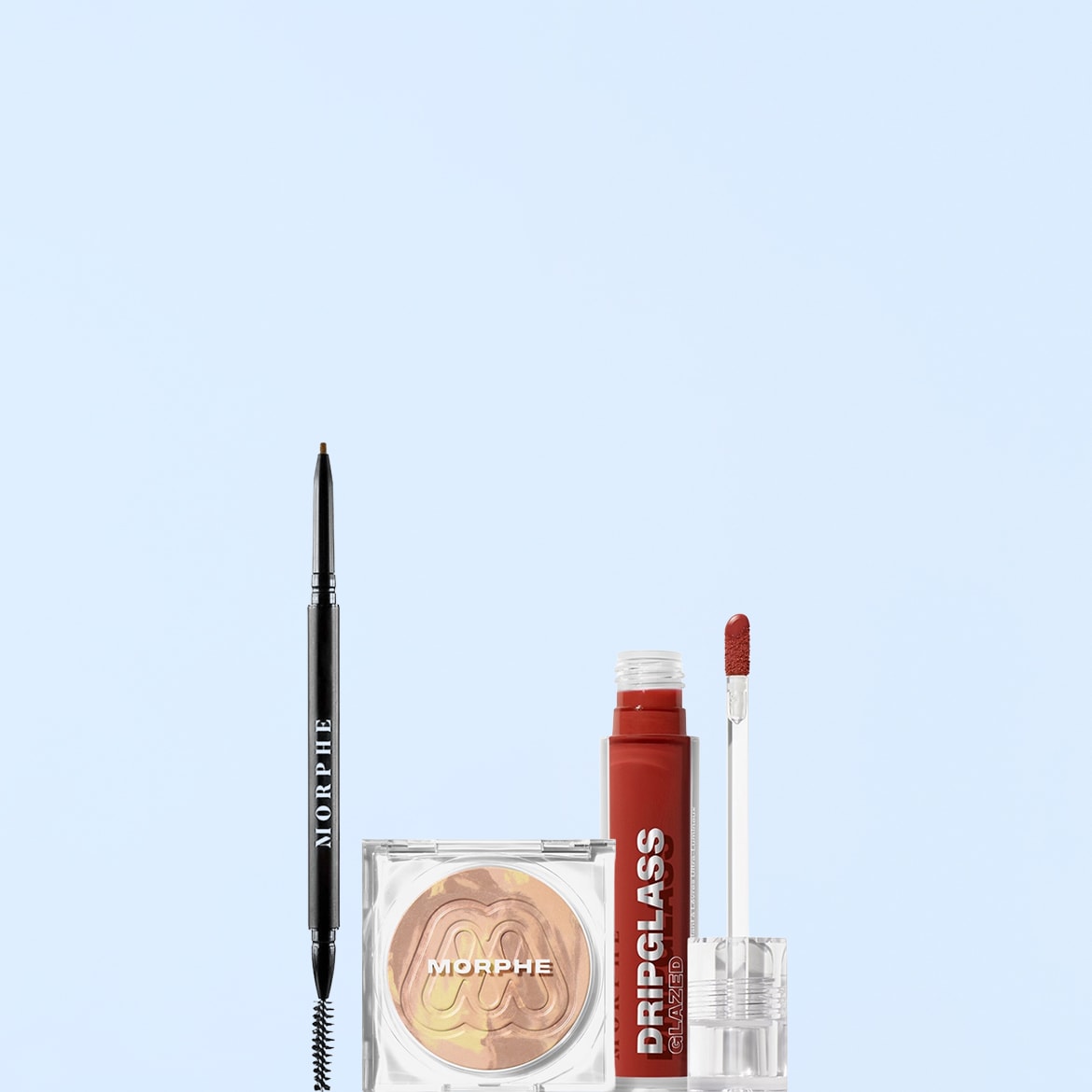 Morphe Dripglass Glazed Lip Gloss in un vivace rosso corallo, un illuminante compatto con sfumature dorate e un matita per sopracciglia marrone scuro con scovolino, tutti su sfondo azzurro.