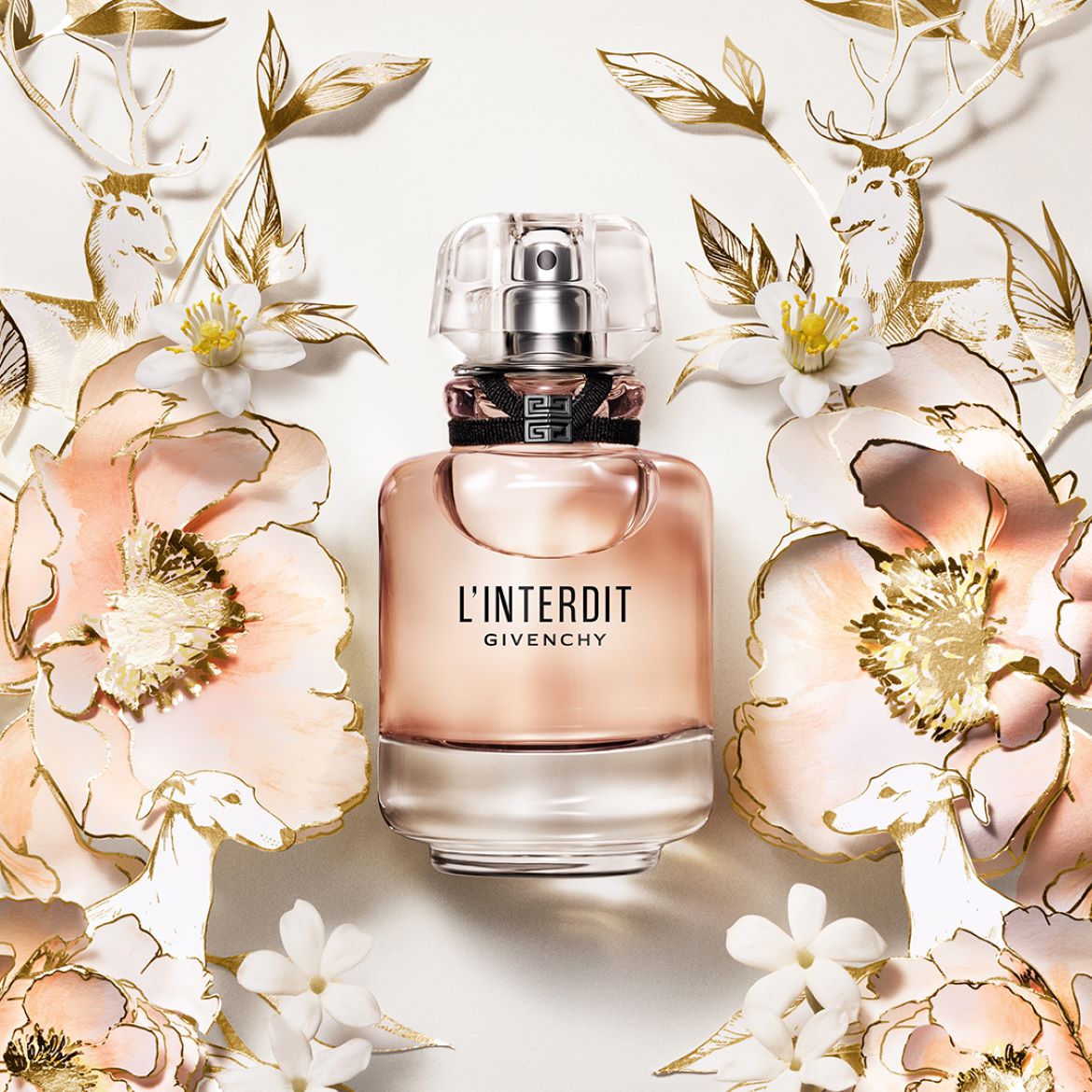 Il profumo L'Interdit di Givenchy è racchiuso in un flacone di vetro rosa chiaro, circondato da fiori di pesco e decorazioni dorate.