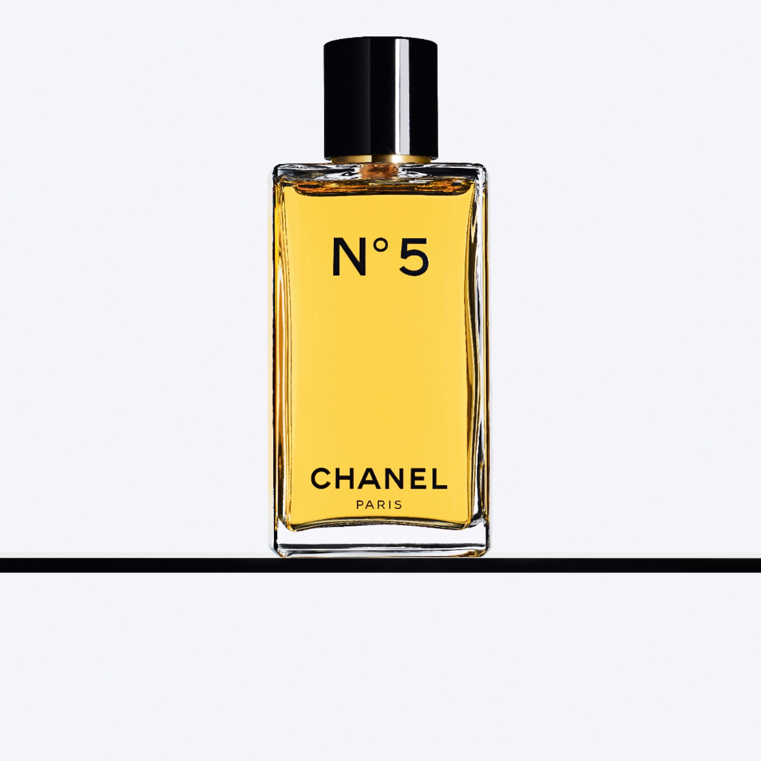 Ecco il flacone di profumo Chanel N°5, con il suo design rettangolare e minimalista, il tappo nero lucido contrasta con il liquido dorato all'interno, un classico intramontabile.