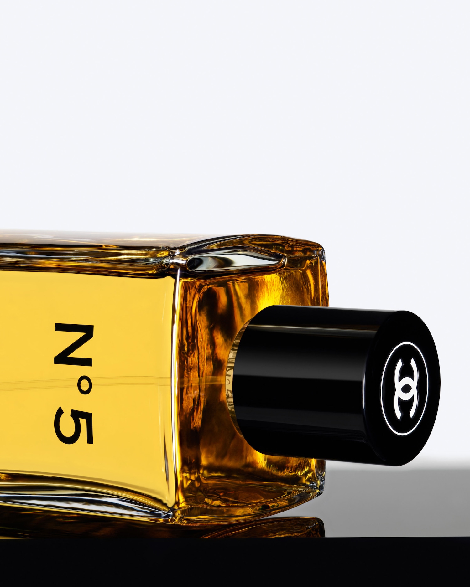 Ecco una bottiglia orizzontale di Chanel N. 5 con tappo nero lucido e logo bianco, piena di profumo dorato.