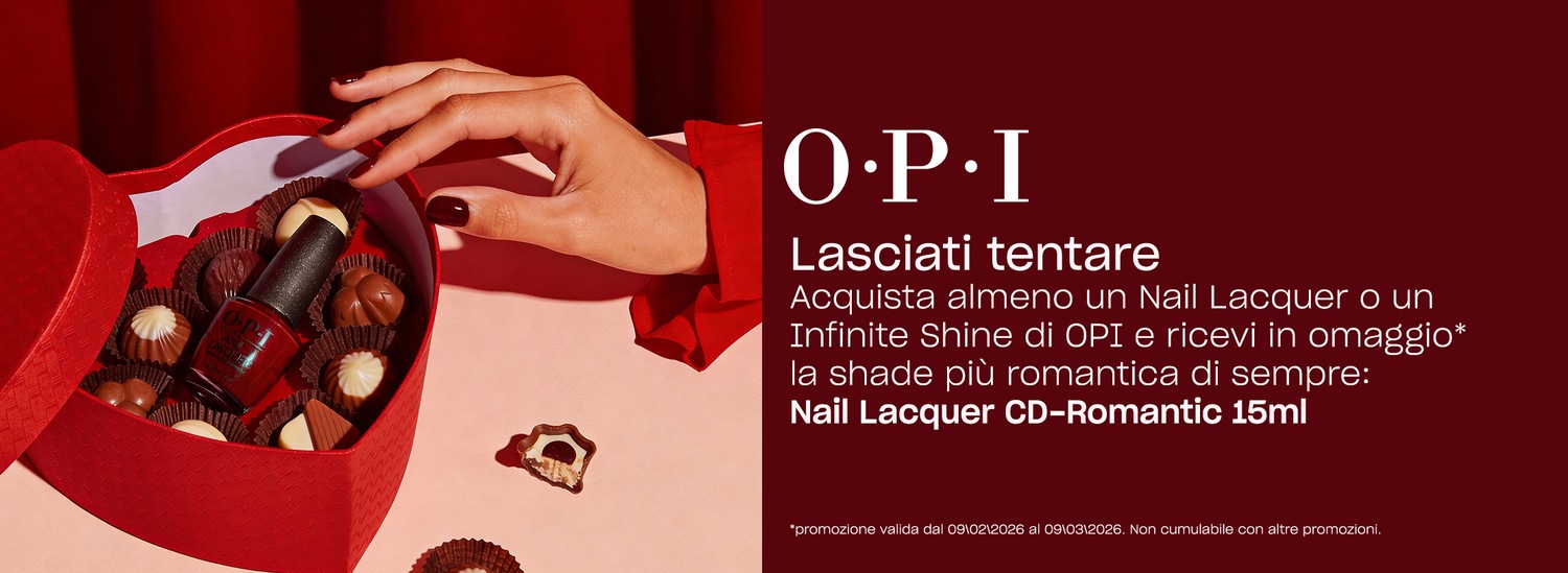 Close-up of a red heart-shaped box filled with chocolates and a bottle of OPI nail polish, with a hand reaching in, promoting a gift of Nail Lacquer CD-Romantic 15ml with purchase.