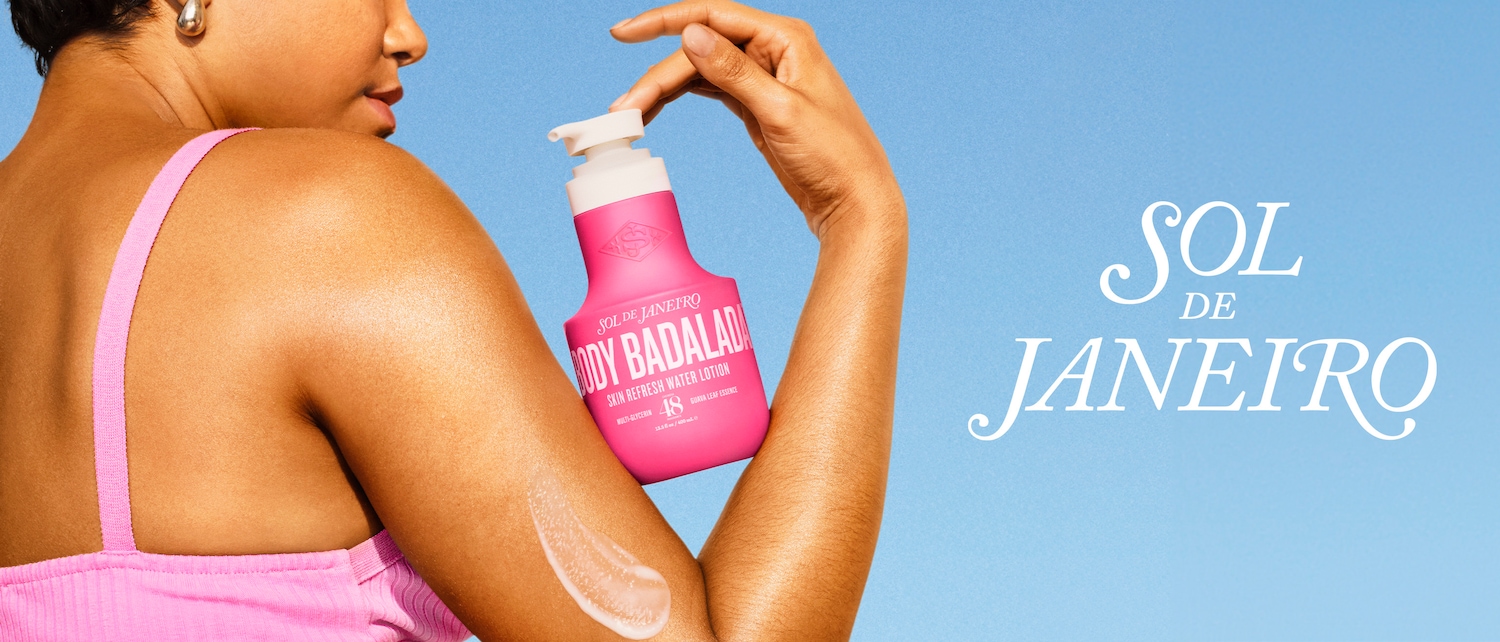 Una donna applica la lozione rinfrescante per la pelle Body Badalada di Sol de Janeiro, confezionata in un flacone rosa con scritte bianche, su uno sfondo azzurro.
