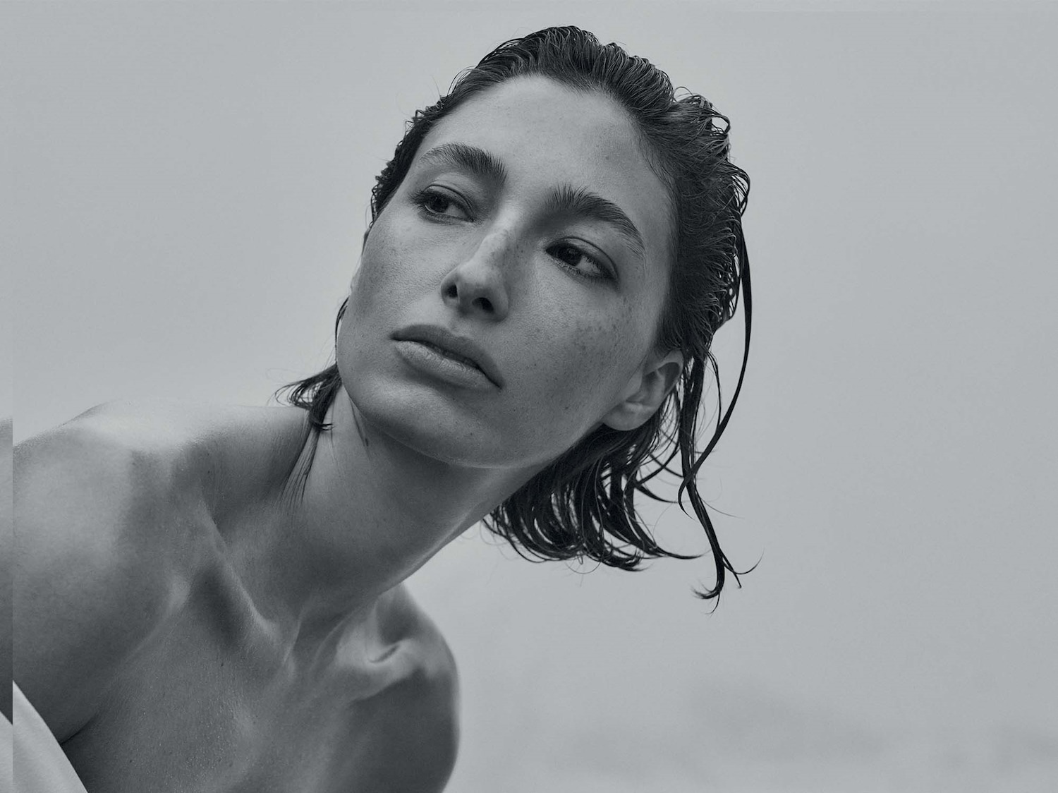 Primo piano in bianco e nero di una donna con i capelli bagnati, lo sguardo rivolto verso l'alto e la pelle liscia.