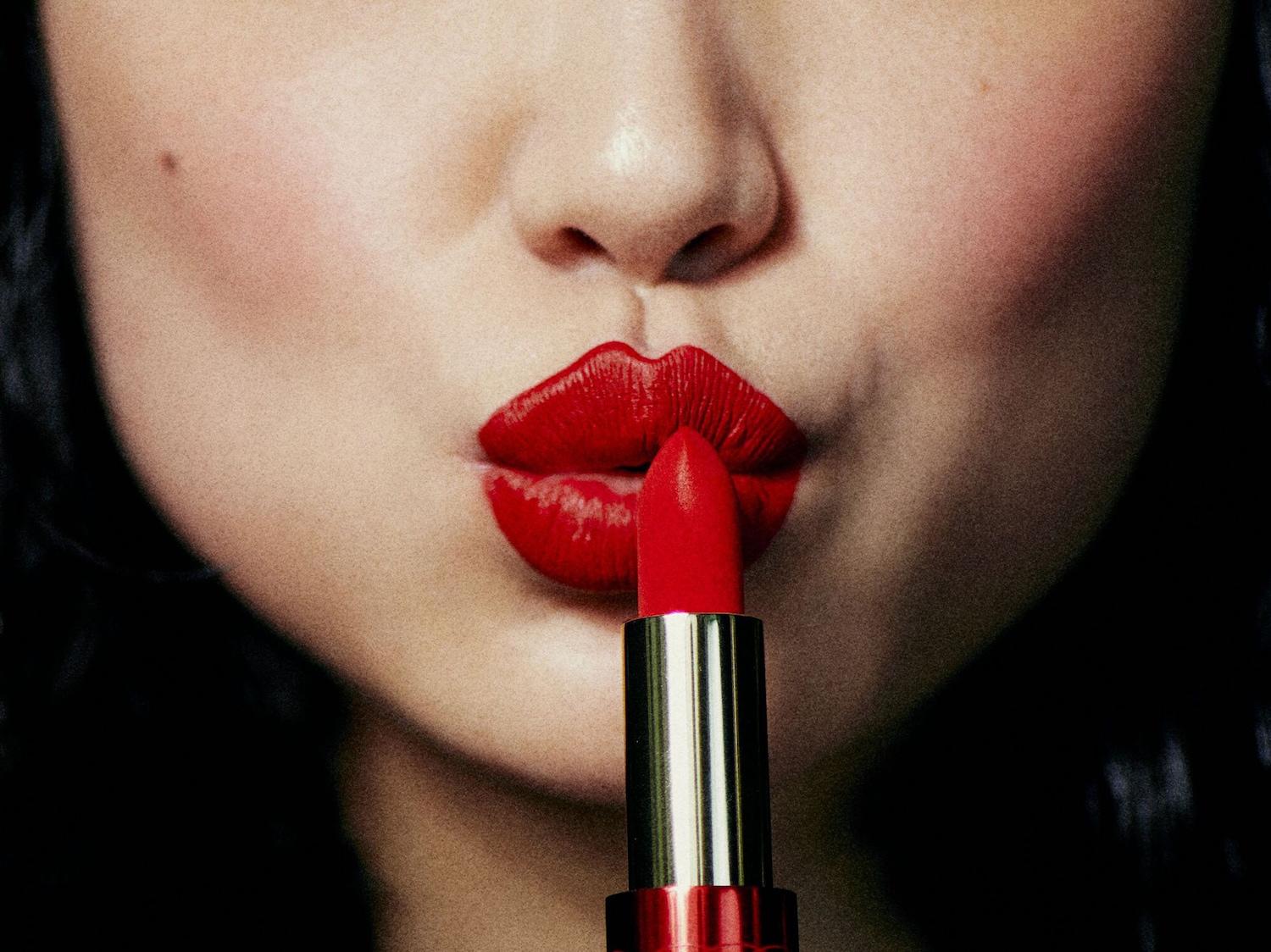 Primo piano di una donna che applica un rossetto rosso brillante sulle labbra, il packaging è dorato e rosso.