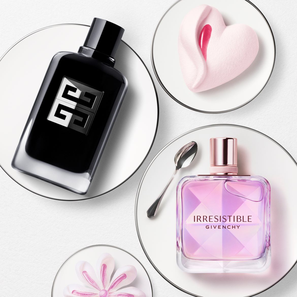 La foto mostra due flaconi di profumo Givenchy, uno nero e uno rosa, presentati su piatti bianchi con decorazioni a forma di cuore e fiore.