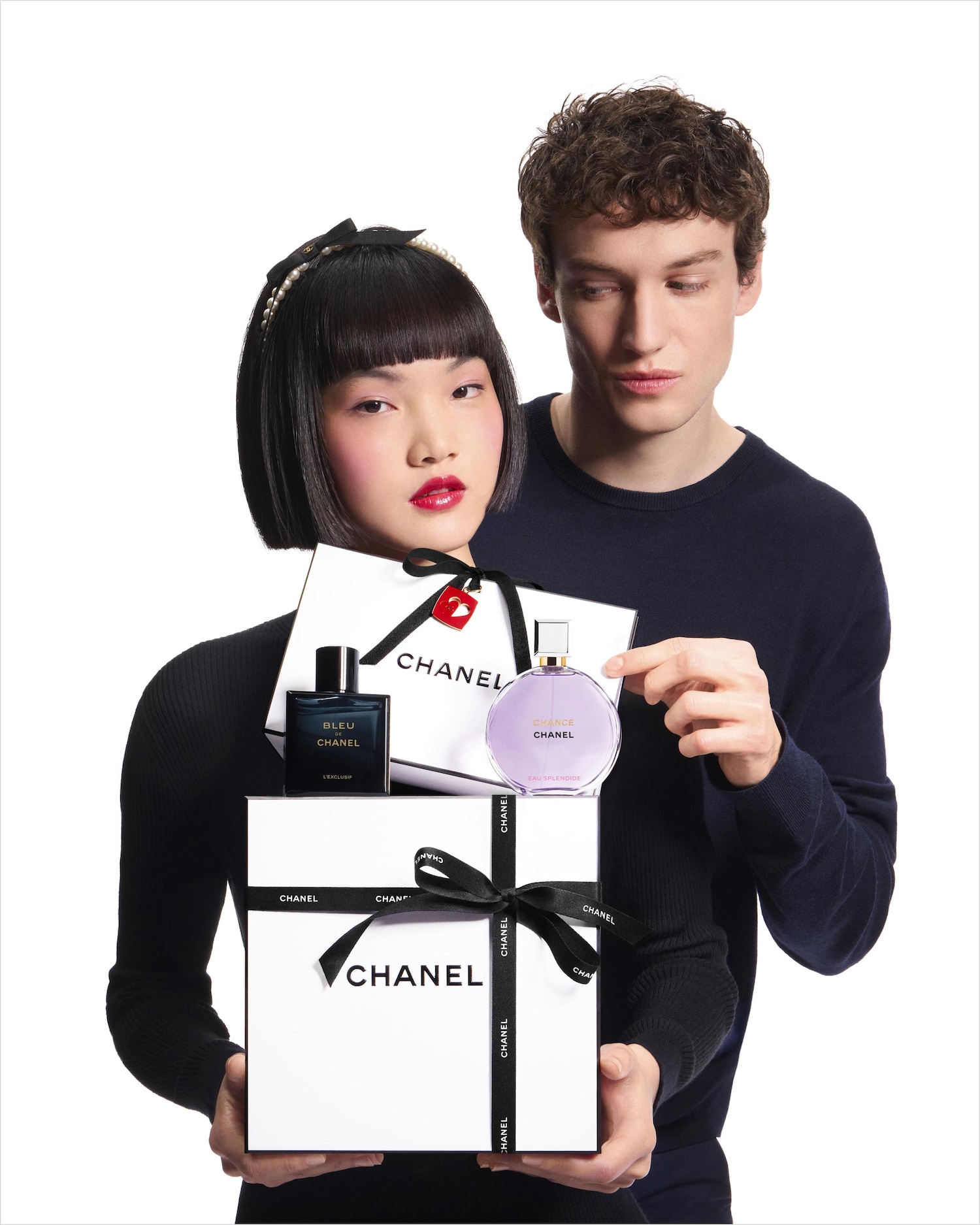 Una coppia presenta una confezione regalo bianca di Chanel legata con un nastro nero, con i profumi Bleu de Chanel e Chance Eau Splendide in bella mostra.
