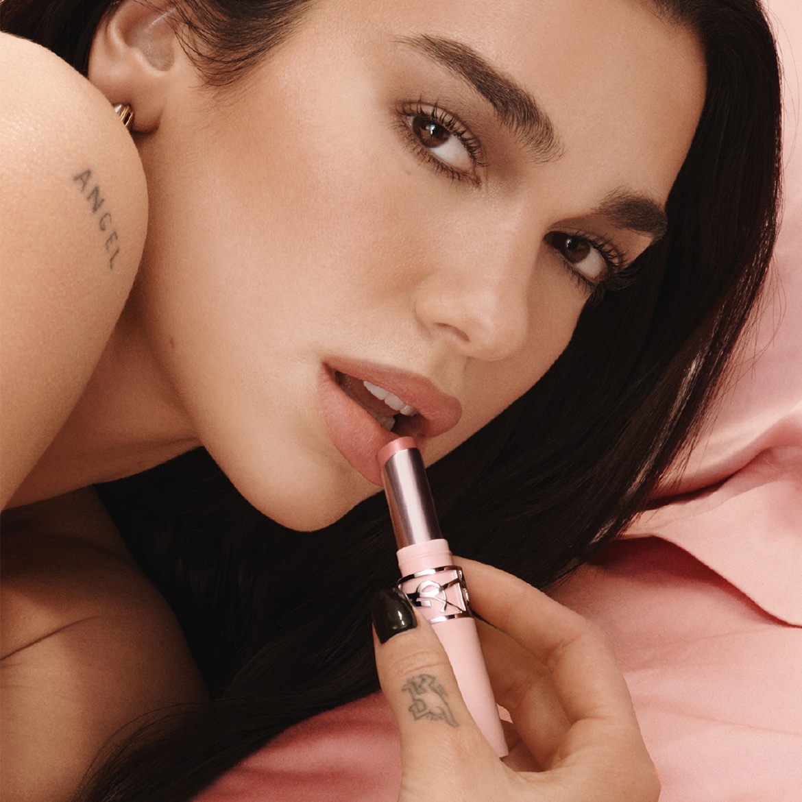 Primo piano di una donna che applica un balsamo labbra rosa chiaro, confezionato in un elegante stick rosa e argento, per labbra idratate e luminose.