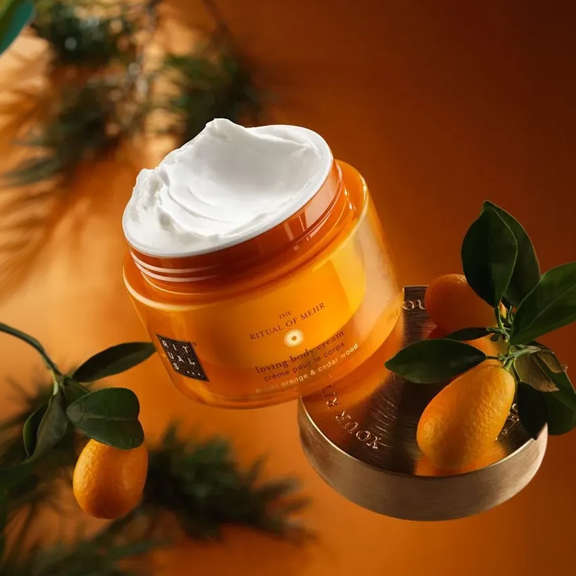 Ecco il Ritual of Mehr loving body cream, un'esperienza sensoriale con crema all'arancia e legno di cedro, presentata in un barattolo arancione con un coperchio dorato.